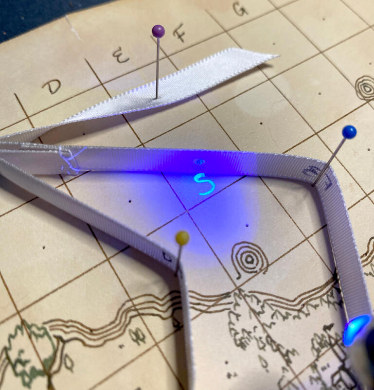 A close up of the pinned ribbon and a secret letter hidden on the map in black light, indicated by a corresponding dot on the back of the ribbon.